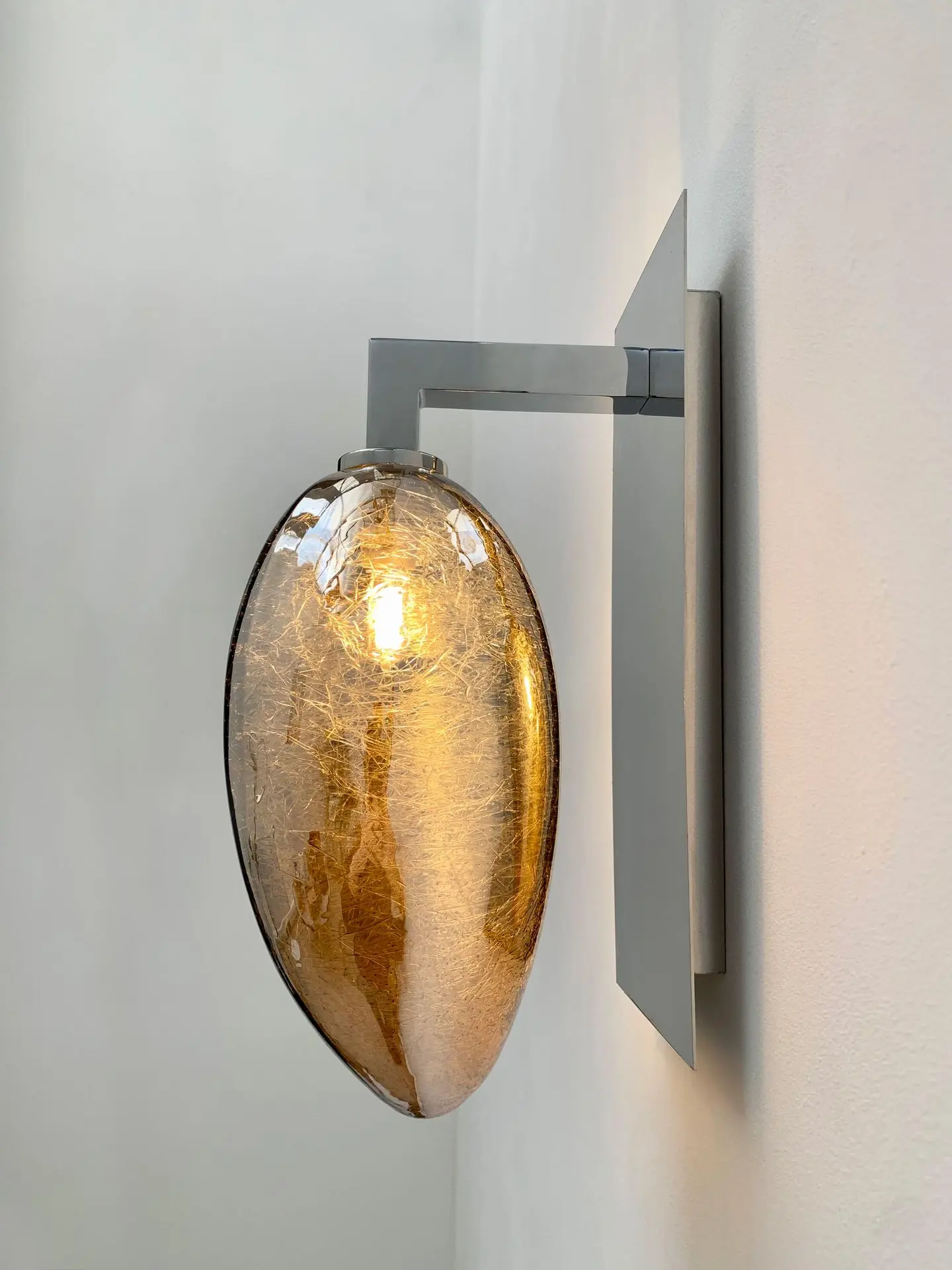 luminaire simple accroché à un mur par un crochet(accroche murale(. Verre restistant a l'humidité de couleur ambre avec des fils argenté à l'interieur forme elliptique