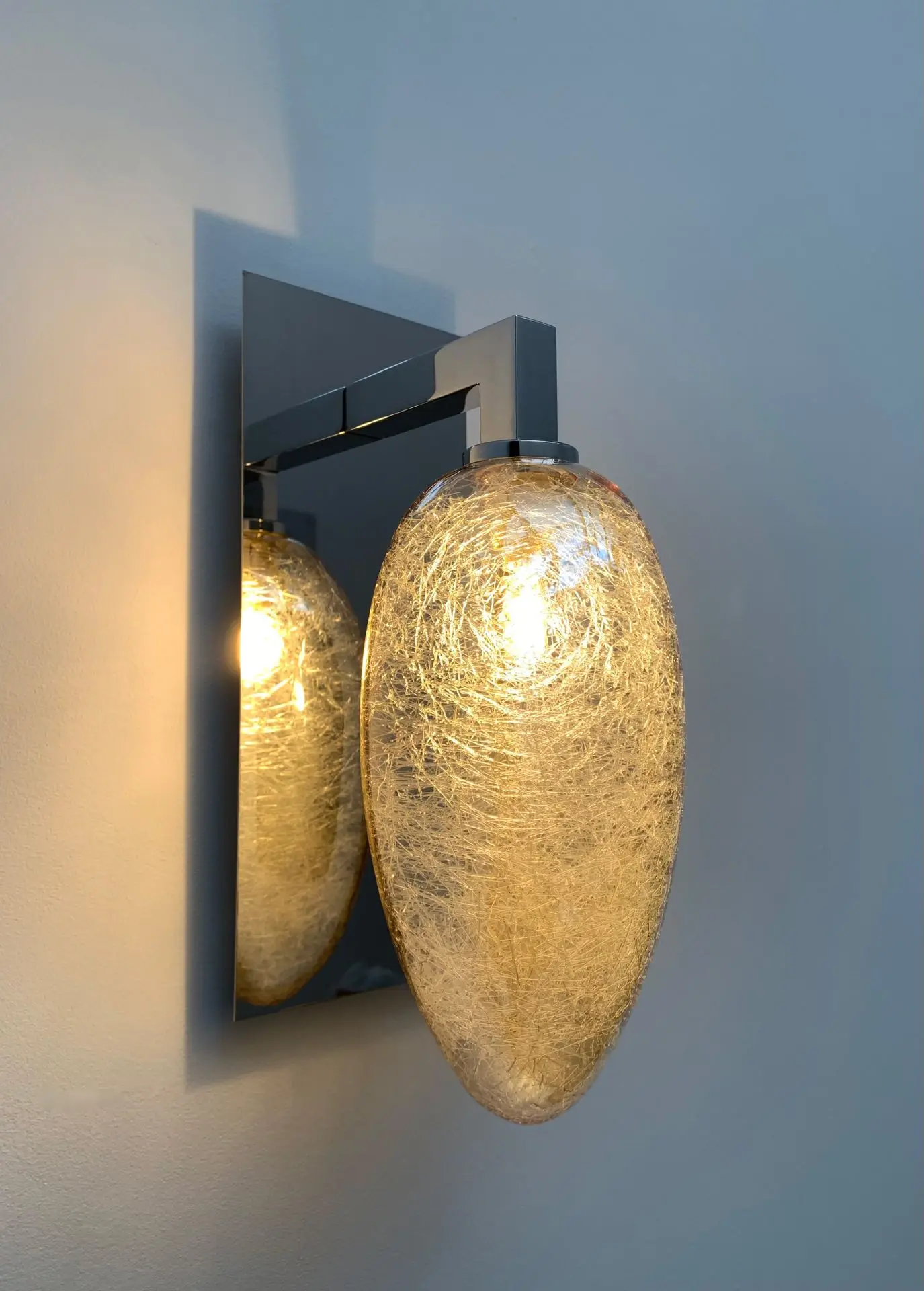 luminaire simple accroché à un mur par un crochet(accroche murale(. Verre restistant a l'humidité de couleur doré avec des fils argenté à l'interieur une forme ovoïde ou elliptique